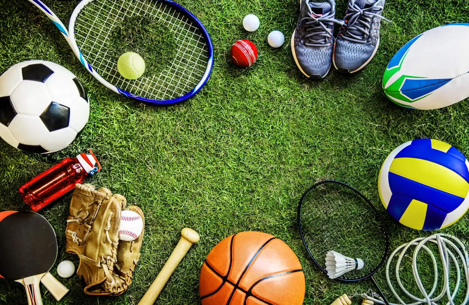 Různé sportovní náčiní na trávníku — fotbal, tenis, basketbal a další